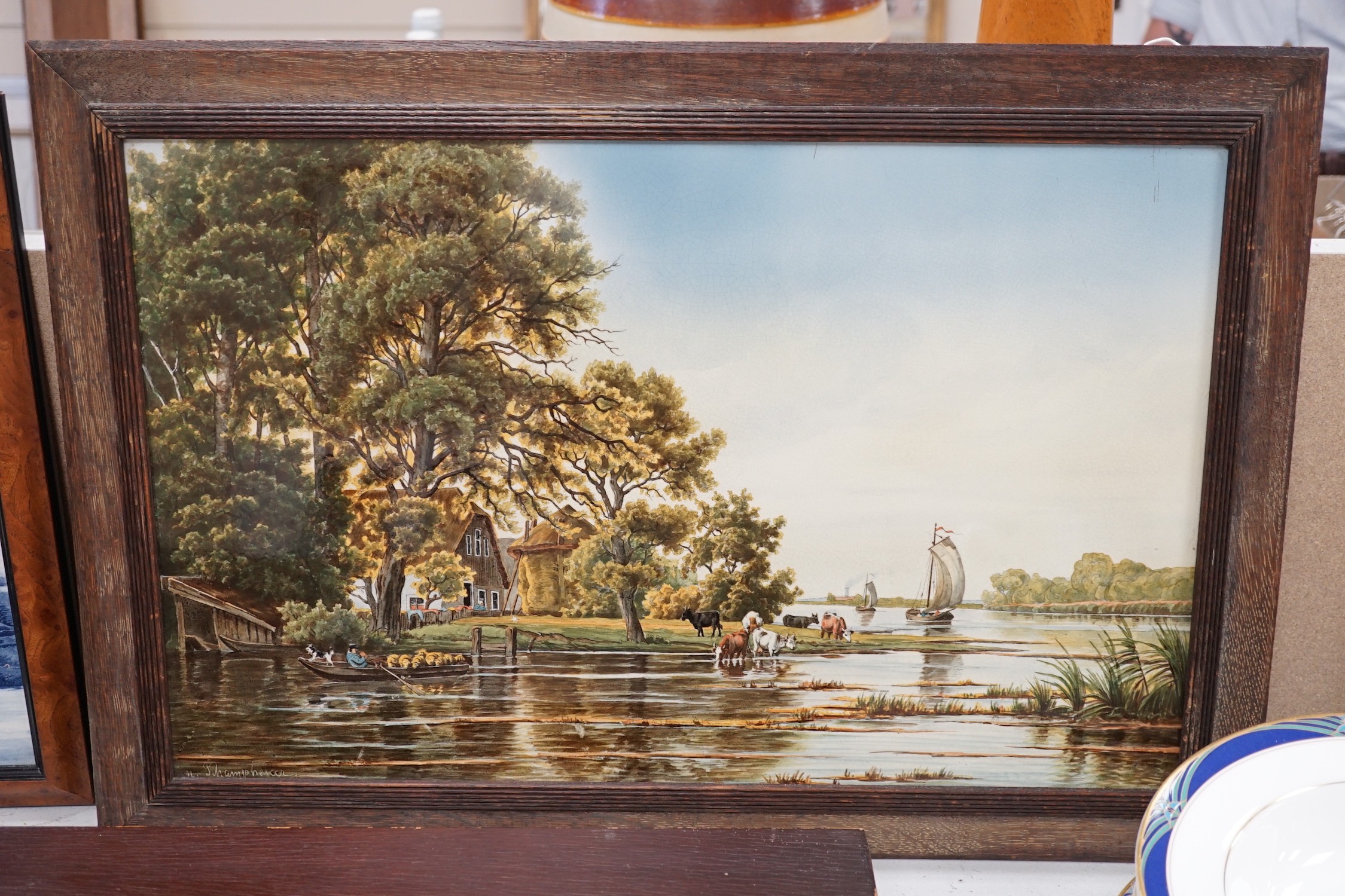 A framed continental ceramic plaque of a figurative country farm river scene, signed, 55cms wide x 35cms high